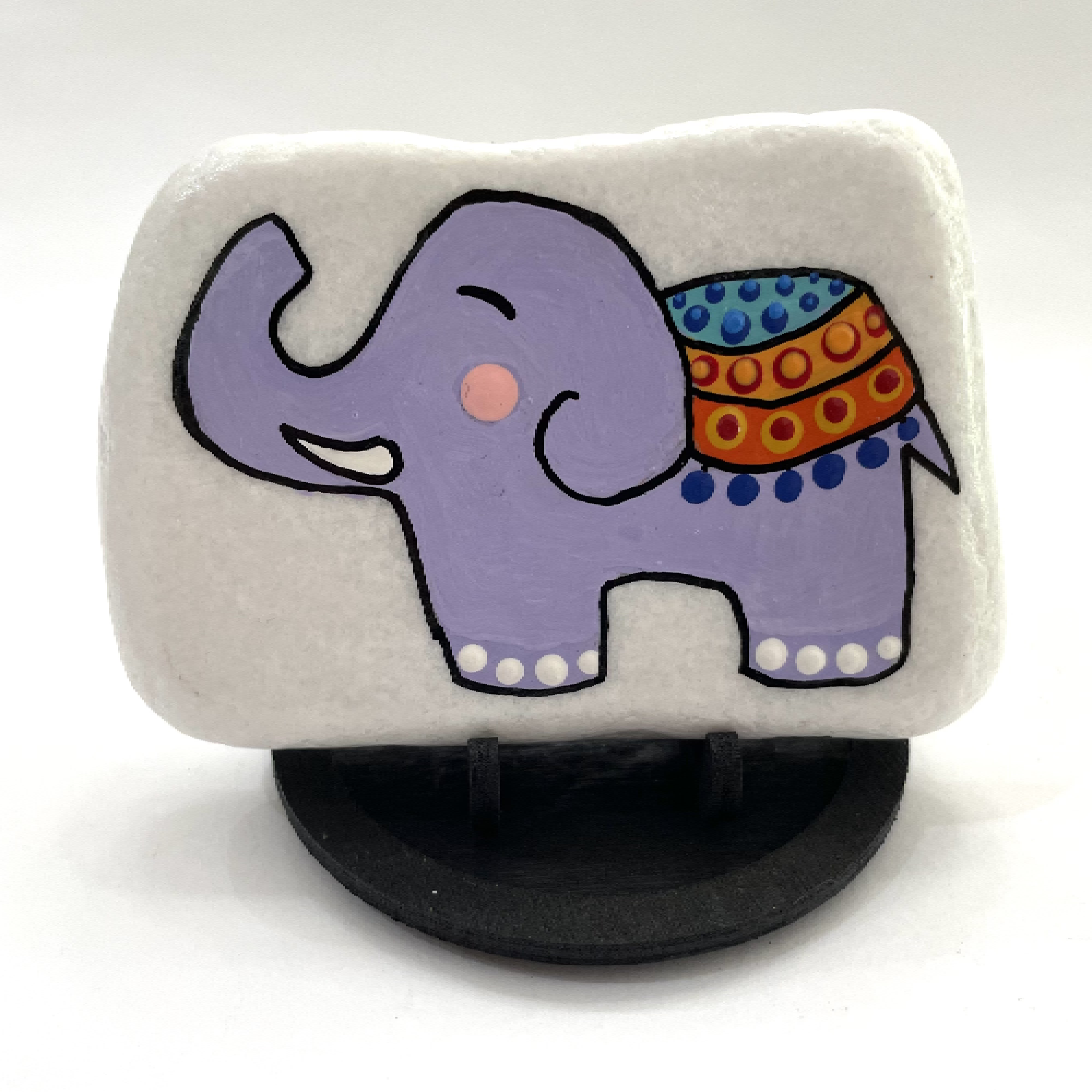 Hand painted purple elephant on a white rock with a decorative blanket, displayed on a black stand